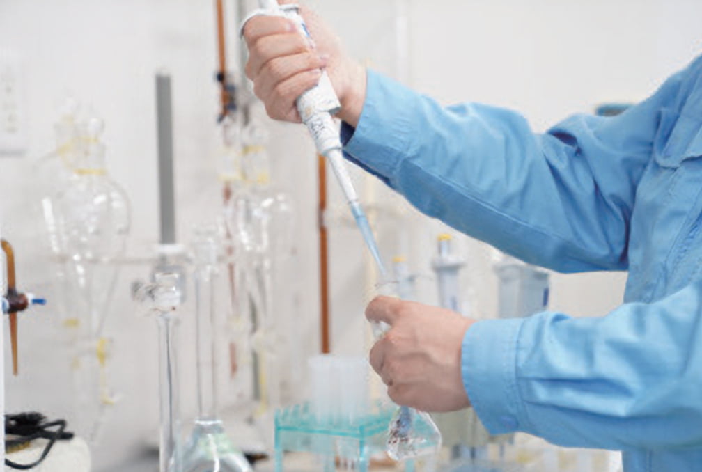 メスフラスコにマイクロピペットで液体を注入している手元の写真